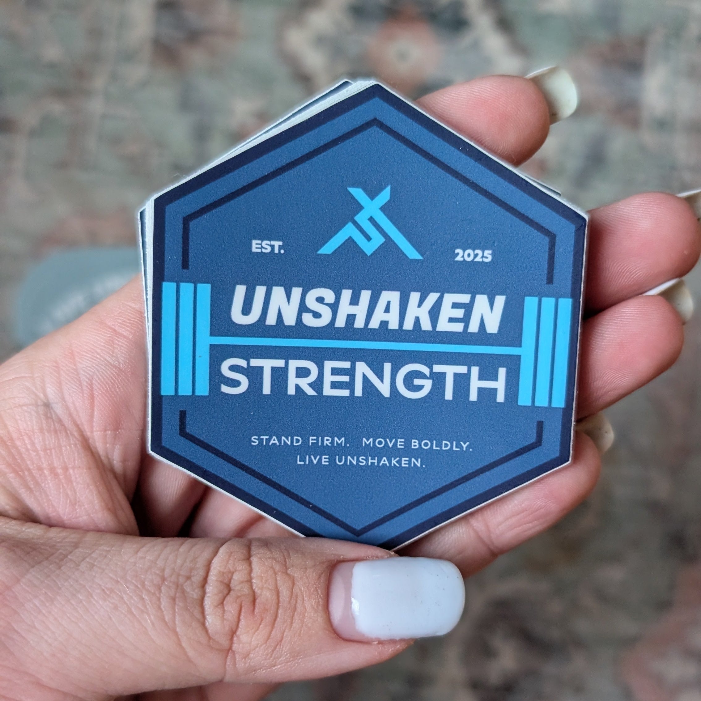 Hexagonal 'Unshaken Strength' badge held in a hand with a patterned rug background