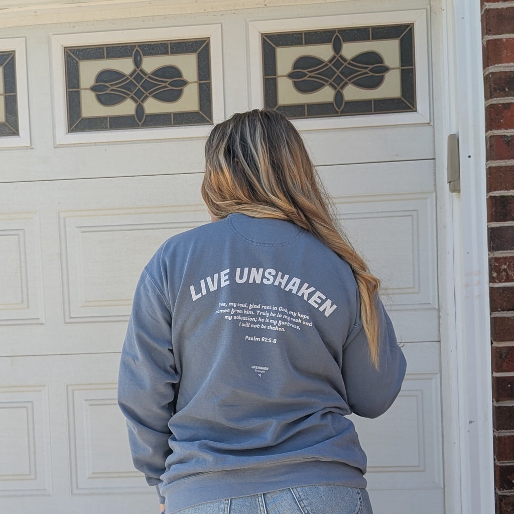 Person wearing a blue sweatshirt with 'Live Unshaken' text, standing in front of a white garage door.