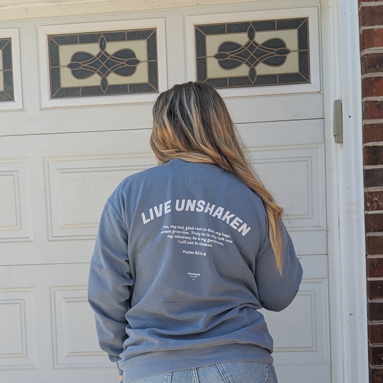 Person wearing a blue sweatshirt with 'Live Unshaken' text, standing in front of a white garage door.