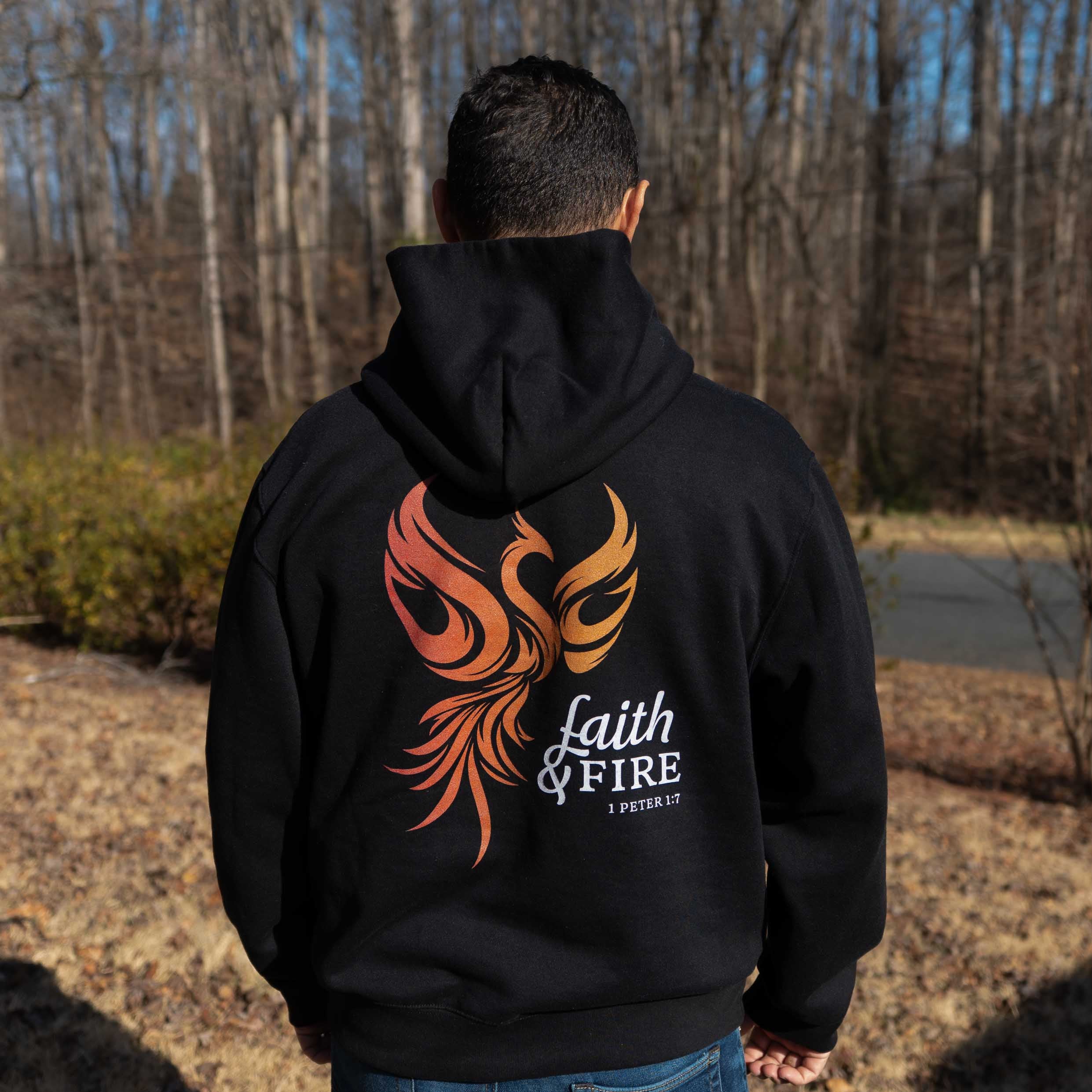 Person wearing a black hoodie with a phoenix design and text outdoors.