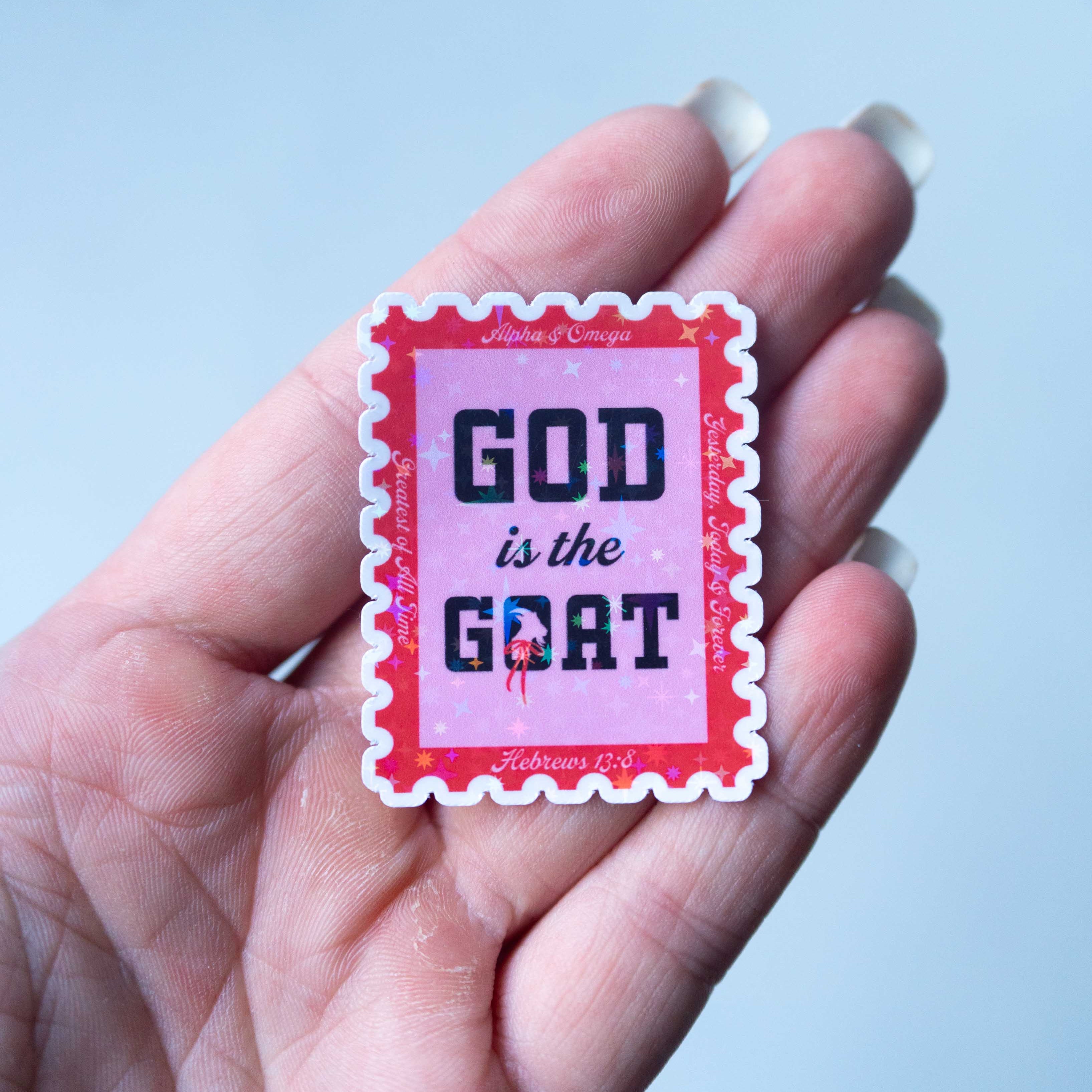 Hand holding a small red and white stamp with 'GOD is the GOAT' text against a light blue background.